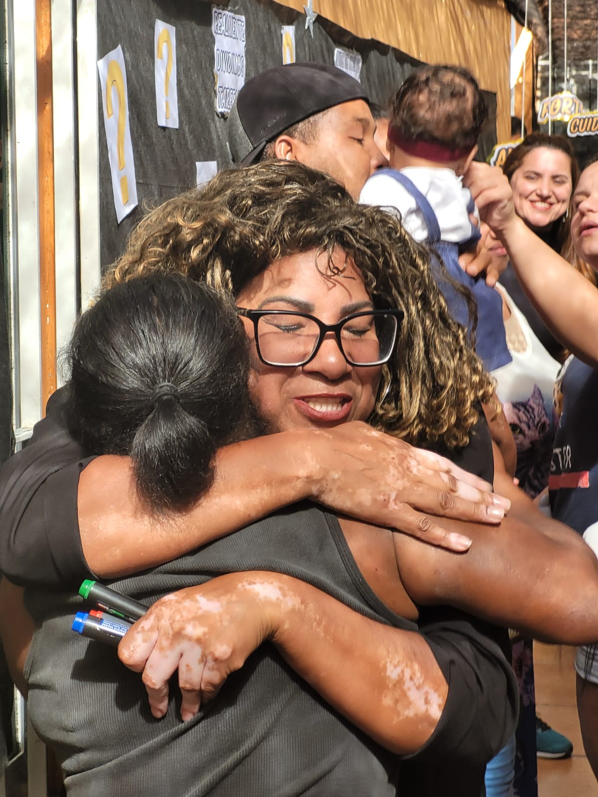 Na imagem, a coordenadora do local, abraça uma participante que se emocionou. Pessoas ao fundo sorriem.